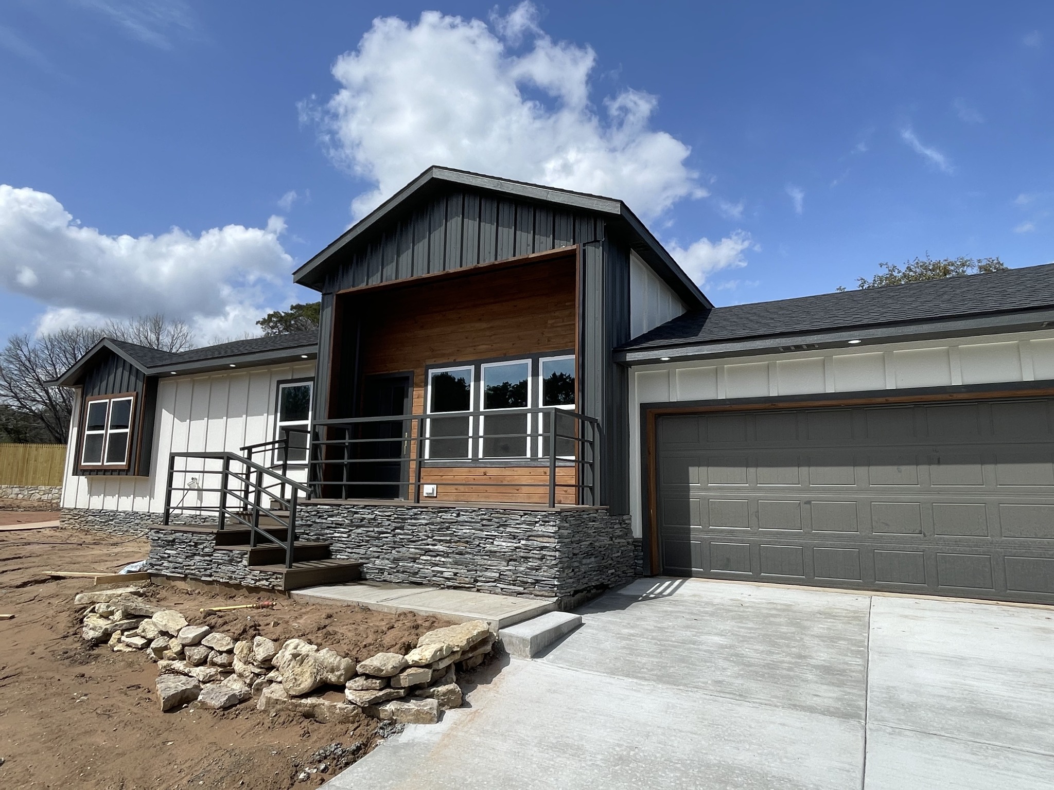 Completed ROI home with a tall wood-accented entry, dark and white siding, stonework and attached garage